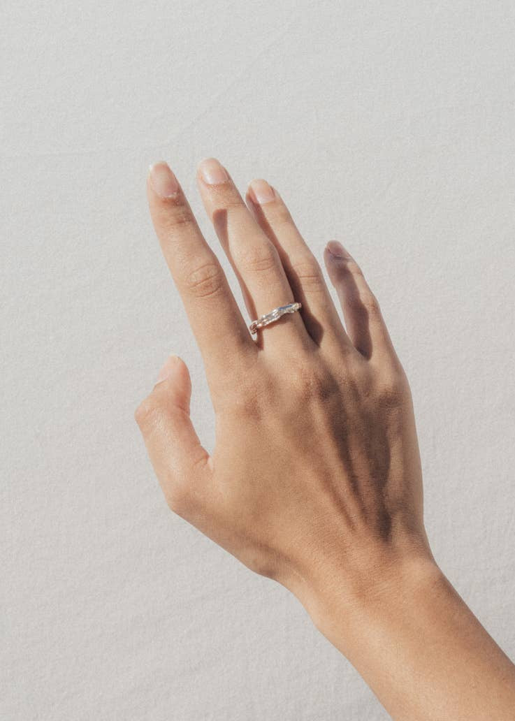 Hand wearing a ring and bracelet on a plain background
